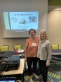 Karen Funkenbusch and another lady in a conference room with a PowerPoint in the background concerning AI for Senior Adults.